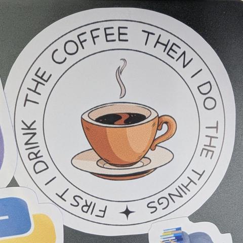 Un sticker circular blanco. En el centro, hay una ilustración de una taza de café humeante de color naranja o terracota, con café oscuro y una pequeña forma ondulada clara en la superficie. La taza descansa sobre un platillo claro, y un par de líneas blancas onduladas representan el vapor que asciende. Rodeando la imagen central, en mayúsculas, se lee el texto en inglés: "FIRST I DRINK THE COFFEE THEN I DO THE THINGS". Una pequeña estrella negra separa la frase en la parte inferior. El mensaje …