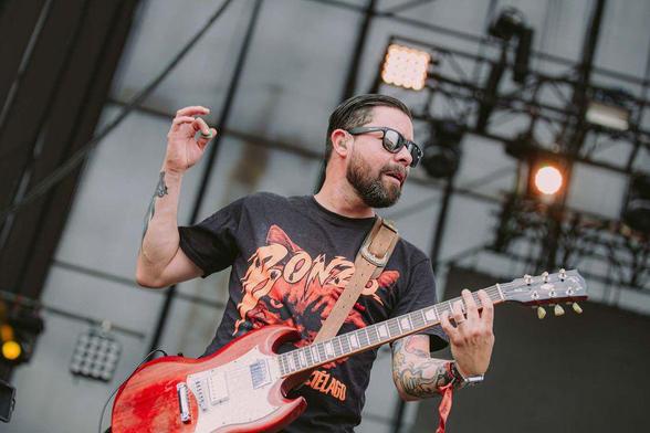 Omar Acosta sobre un escenario tocando la guitarra eléctrica. Viste una polera negra con el logo de su banda Bonzo.