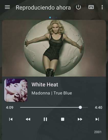 Una pantalla de aplicación de música que muestra una canción de Madonna reproduciéndose.

La imagen principal, que sirve de portada o fondo, muestra a Madonna con cabello rubio rizado, vestida con un body negro transparente y botas altas del mismo color. Está de pie con los brazos extendidos, apoyándose en una gran esfera blanca o gris claro que parece un globo terráqueo texturizado.

Debajo de esta imagen, en la interfaz del reproductor, se ve una miniatura de la portada del álbum "True Blue",…