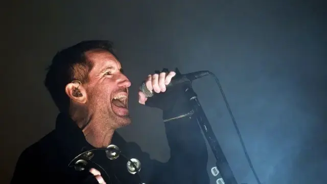Trent Reznor canta con el micrófono en la mano.